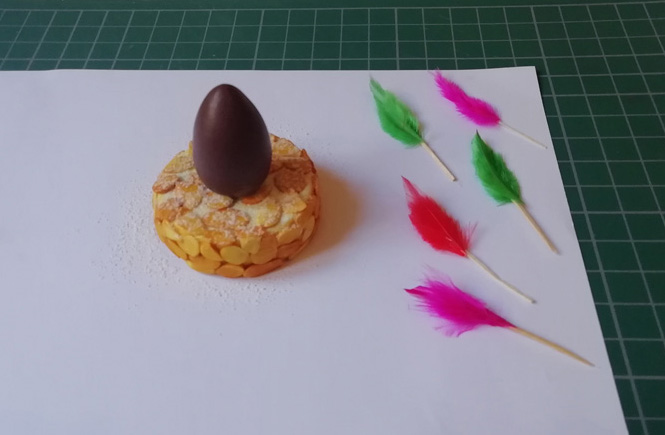 El huevo de chocolate aparece pegado al pastel y cinco plumitas listas para colocar